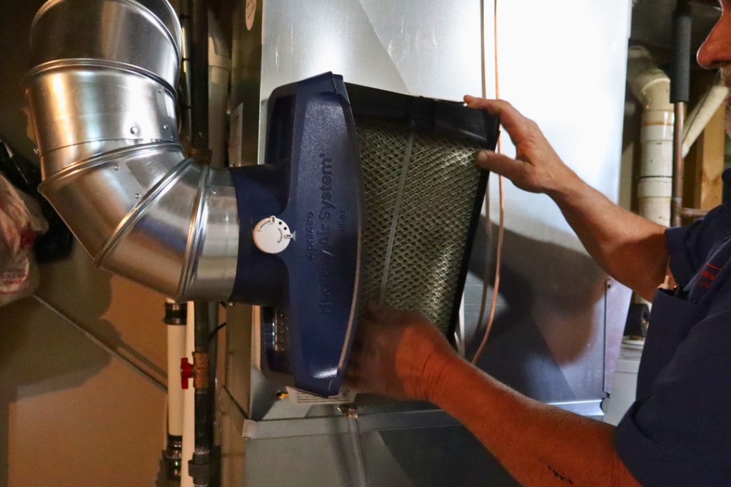 Midwest Comfort technician replacing a whole-home air filter in a basement HVAC system